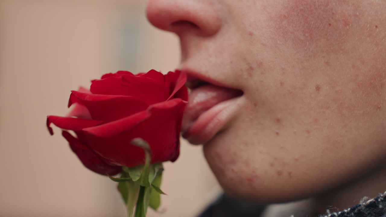 Creatore bianco che lecca una rosa rossa, atto provocatorio di artista di strada, personaggio performer che stuzzica la texture dei petali, primi piani spontanei della bocca, atmosfera sensuale audace, profondità di campo ridotta e luce naturale soffusa, atmosfera urbana.
