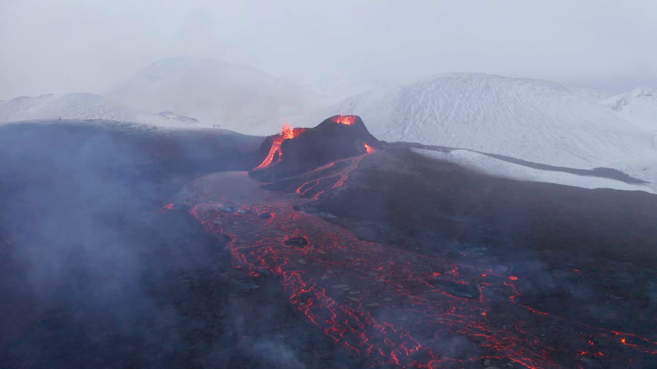 Flyver mod udbrudte vulkankratere ved Fagradalsfjall med sneklædte tinder i baggrunden på Reykjanes-halvøen i Sydisland