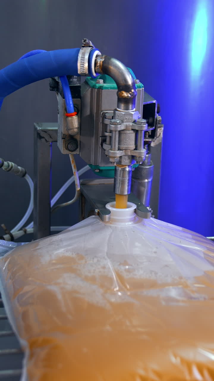 Big transparent plastic bag is filled with organic juice from the automatic machine. Apple juice manufacturing at the plant. Close up. Vertical video