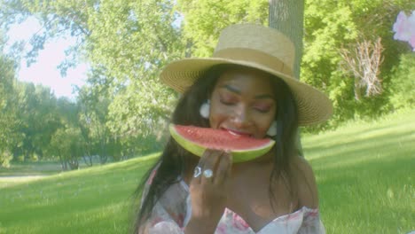 slomo frontal de dama negra en un picnic tomando un bocado de una gran rebanada de sandía