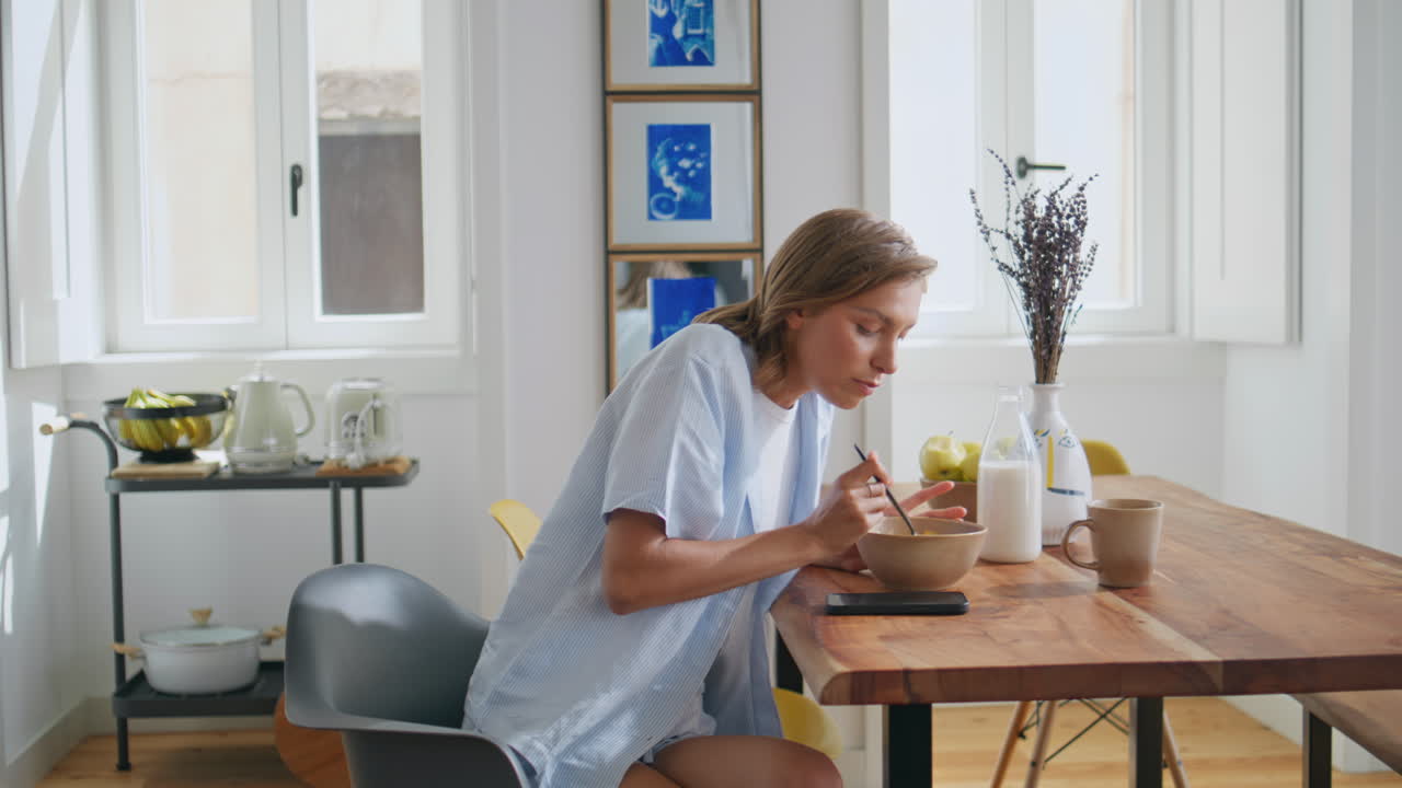 Girl answering morning call in kitchen. Relaxed woman eating breakfast talking