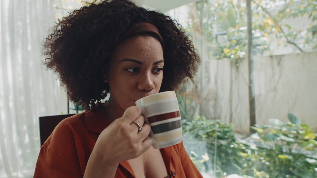 Woman Drinking Coffee while Analyzing Business Charts on Laptop at Home