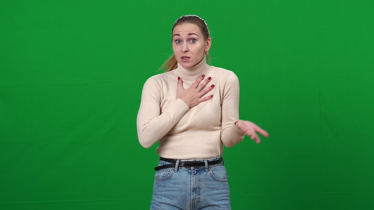 Shocked young woman excusing herself at chromakey background. Middle shot portrait of slim beautiful Caucasian lady making excuse defending on green screen