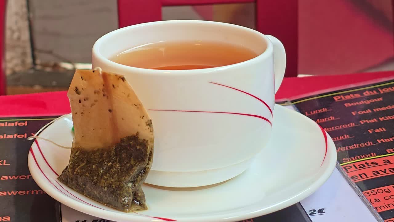 Static close-up shot of a white cup of tea with a teabag on the saucer, placed on a restaurant table
