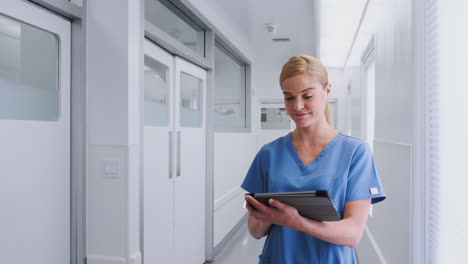 Female-Doctor-Wearing-Scrubs-In-Hospital-Corridor-Using-Digital-Tablet