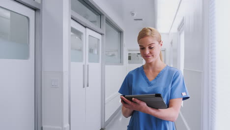 female doctor wearing scrubs in hospital corridor using digital tablet