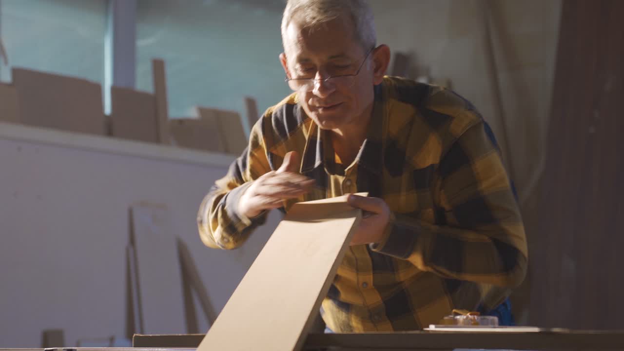 el maestro carpintero sopla el polvo de la madera, la limpia.