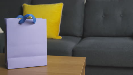 close up of man picking up gift wrapped present in bag from table in lounge at home