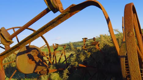 old farm cultivator rusting in field on sunny day. historic piece of farming equipment decaying from past agricultural era. filmed in wales uk.