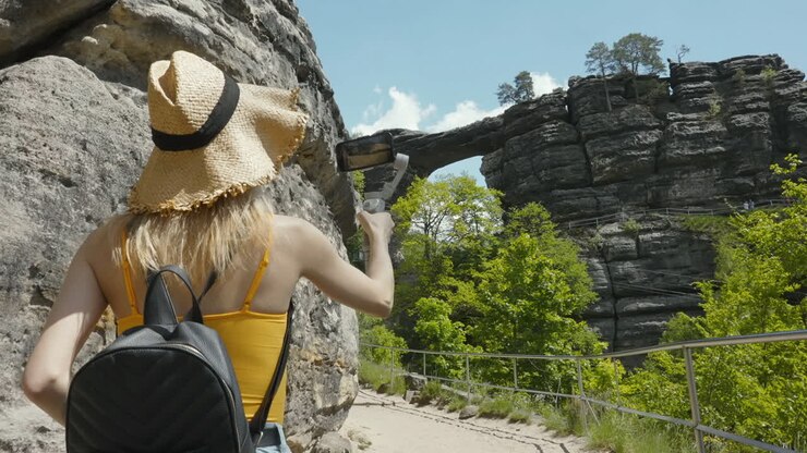 Espalda de mujer joven en sendero de senderismo grabando video de viaje para vlog en paisaje escénico en un día soleado de verano, cámara lenta