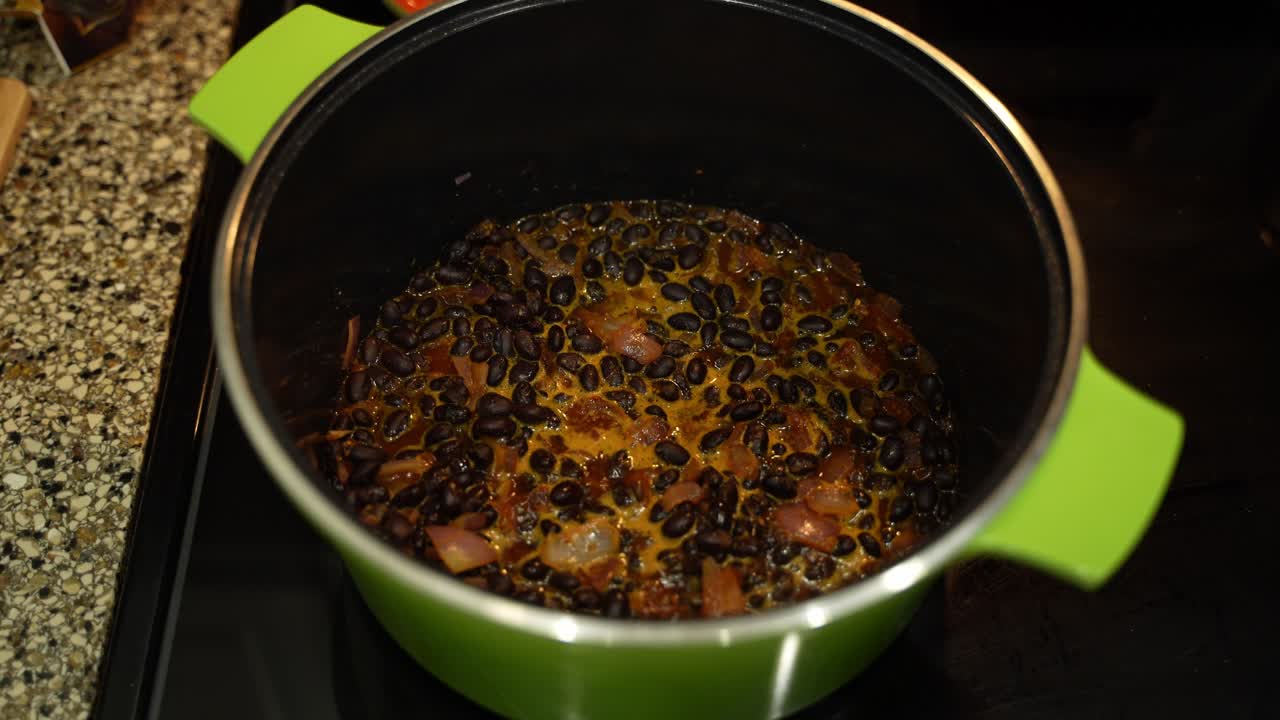 Medium shot of beans and onions boiling in a metal pot on the stove for a tasty meal