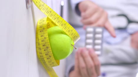 vertical video of doctor holding medicine blister pointing to apple wrapped in measuring tape, diet concept