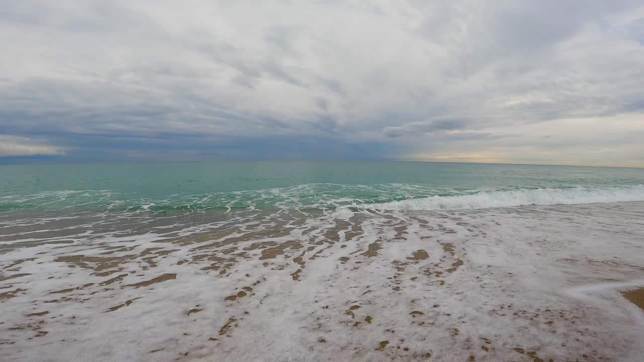 ola de mar de playa de arena gruesa en cámara lenta a 120fps 4k día nublado agua turquesa olas de mar individuales gran playa vacía