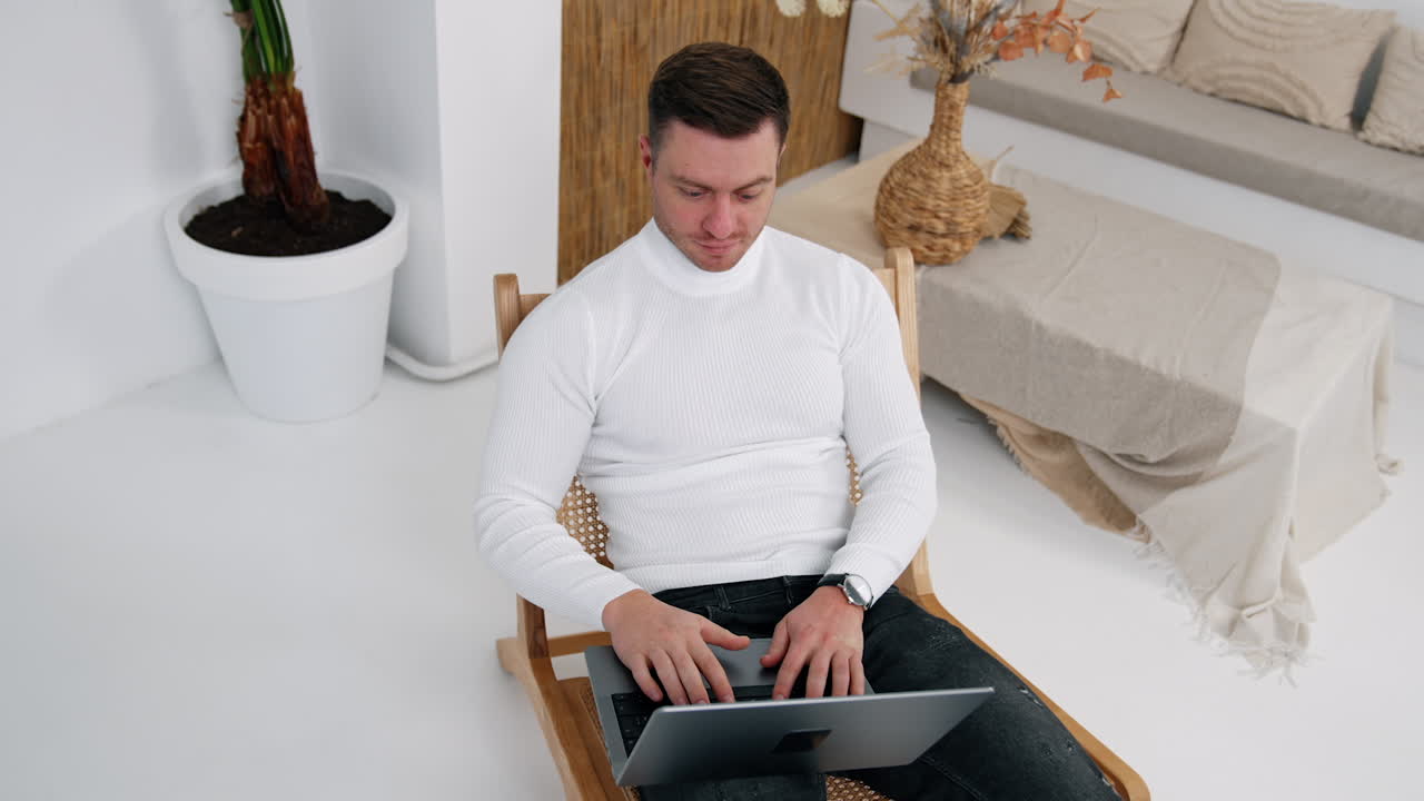 Handsome male in white shirt opens laptop and starts working. Top view on the entrepreneur freelancing from home.