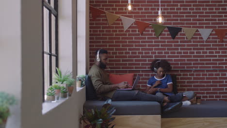 young african american business students study together working on creative project brainstorming ideas listening to music wearing headphones in modern office workplace