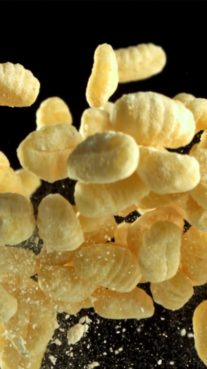 Gnocchi crudi che fluttuano al rallentatore con polvere di farina su sfondo nero