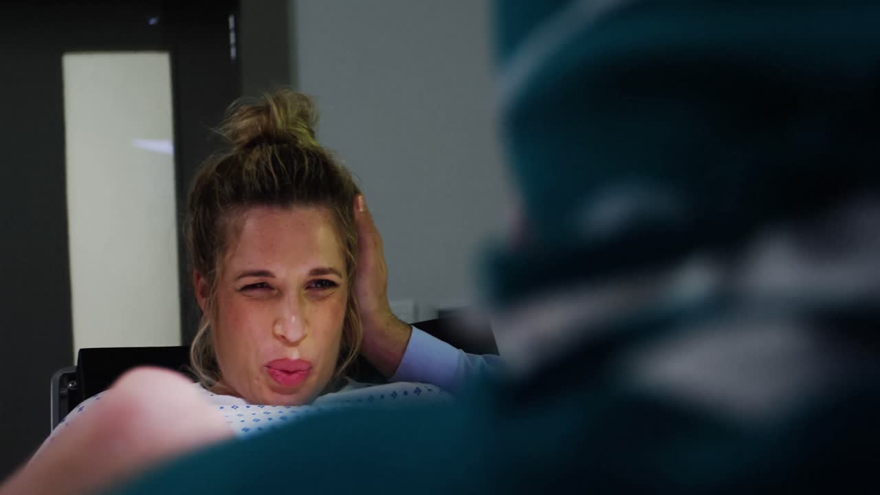 médico examinando a una mujer embarazada durante el parto mientras el hombre la sostiene de la mano en la sala de operaciones