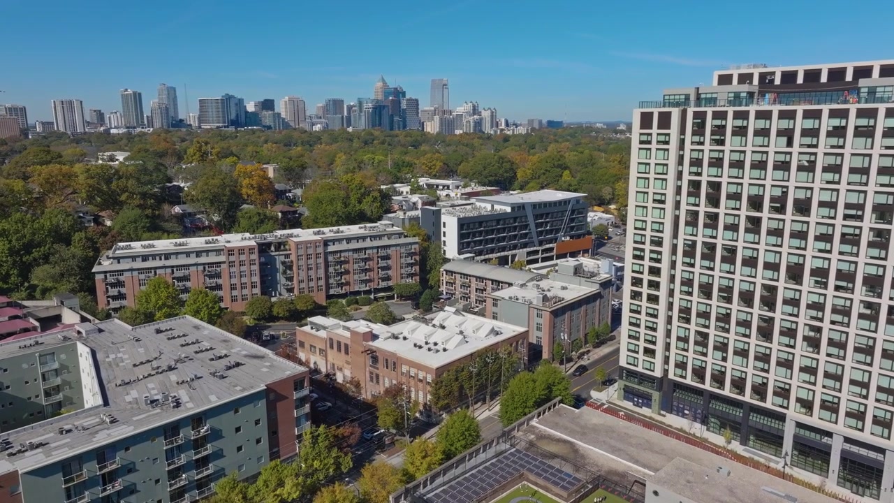 Zona residenziale suburbana con condomini e case in un quartiere signorile di Atlanta. Skyline del centro con grattacieli contro il cielo blu in lontananza. Alberi con fogliame autunnale. Ampia ripresa aerea