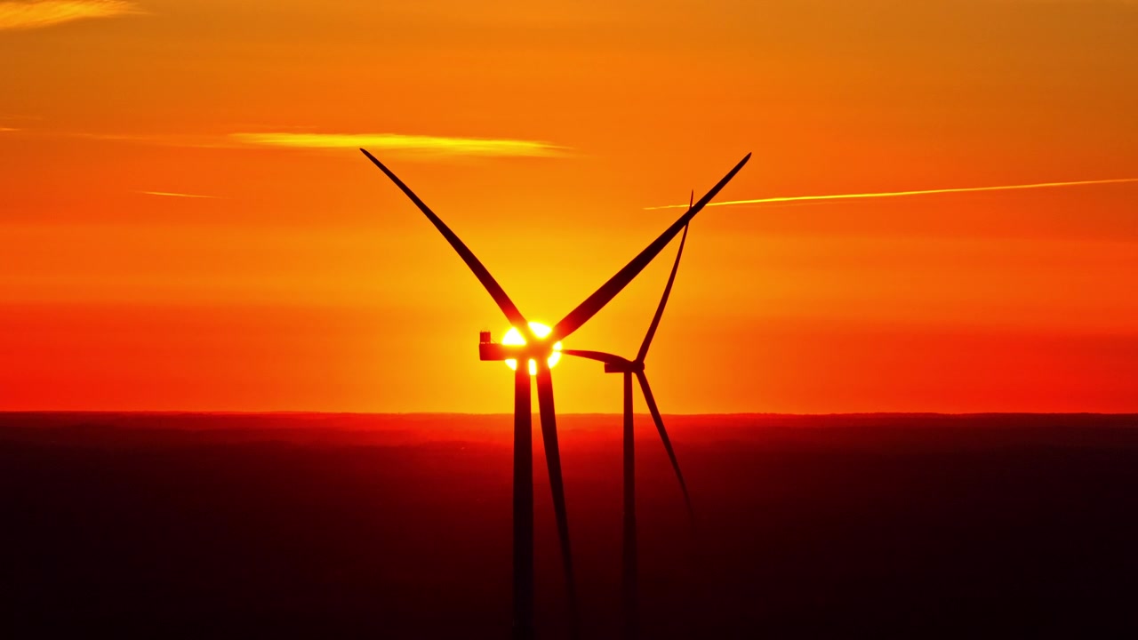 Rotierende Windturbinen als Silhouette vor einem leuchtend orangefarbenen Himmel bei Sonnenuntergang zur Energiegewinnung.