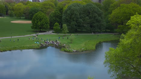 High-angle-view-of-people-relaxing-on-pond-shores-of-Central-Park-in-New-York,-United-States-of-America