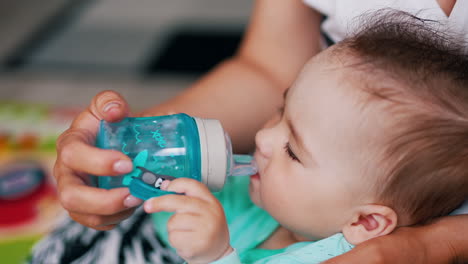 baby drinking water from a plastic bottle with pacifier. mommy holding a bottle for her son. close up.
