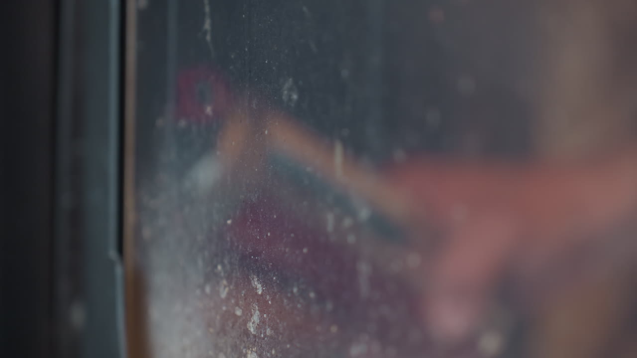 Blurred reflection of person holding object behind dusty stained glass surface, motion and activity partially visible through textured pane, creating mysterious abstract visual