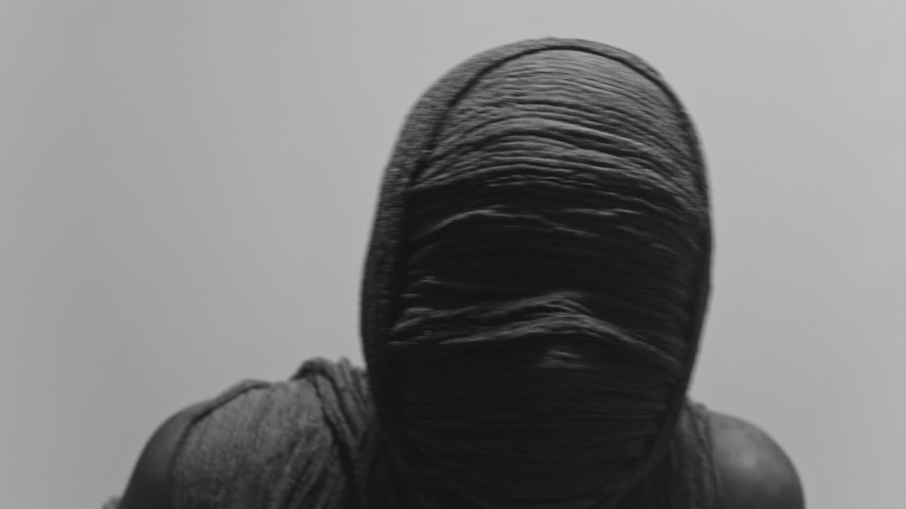 A mummy of a woman on a white backdrop rises her head