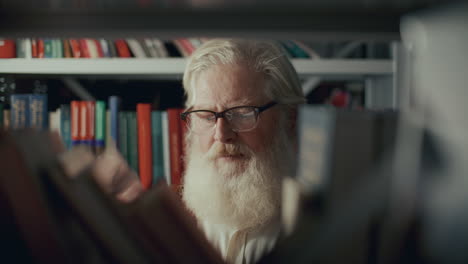 elderly man in glasses looking for book to read in library