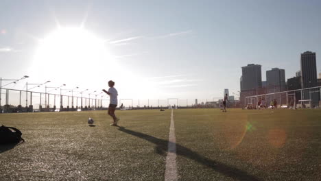 wide shot of girl silhouetted juggling soccer ball with sun and cityscape