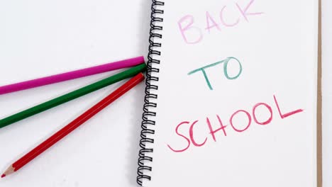 back to school text on open diary with colored pencils
