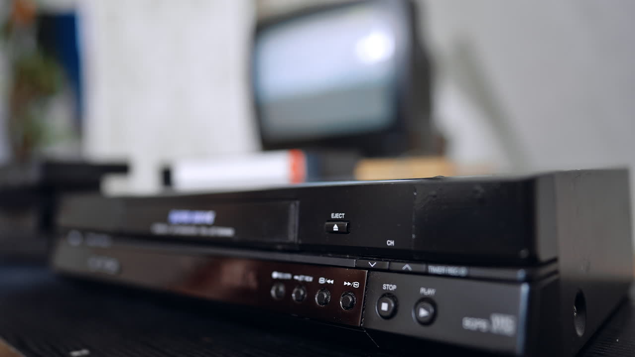 Hand presses the buttons on the panel of the DVD player. Close up. VHS tape appears and hand takes it away