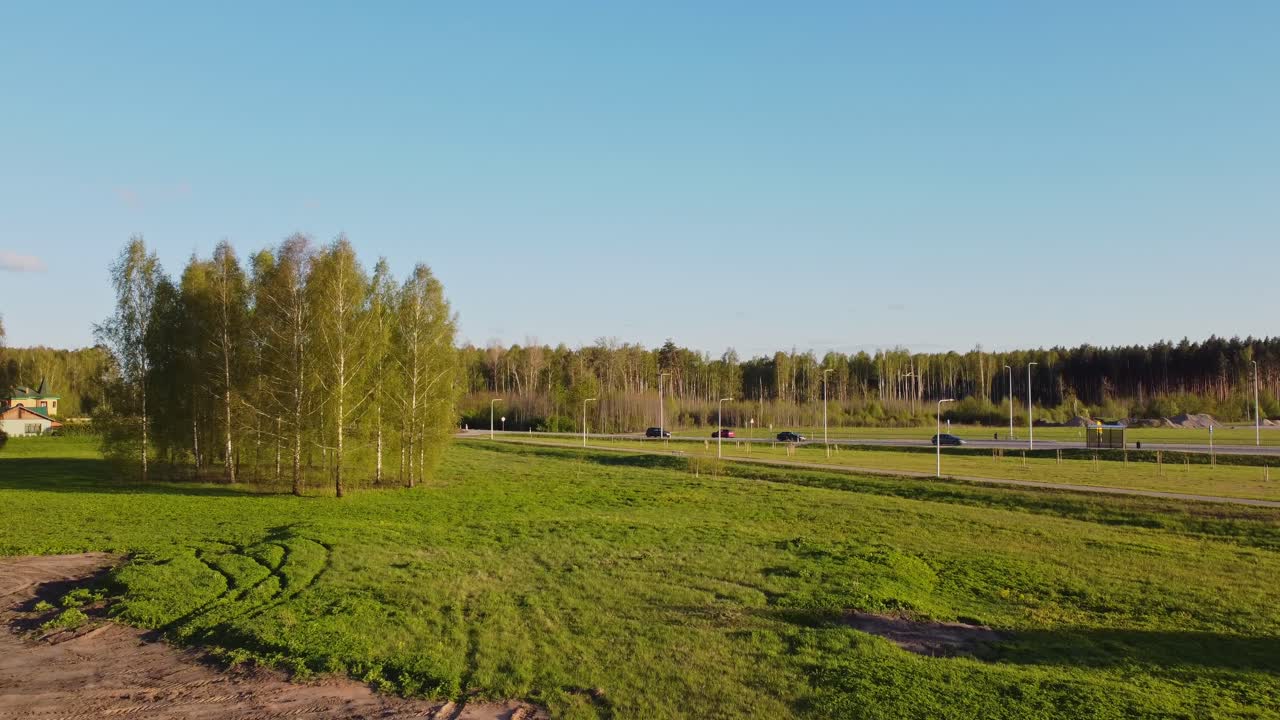 Katlakalns grassland in springtime showing silver birch trees and tracks in foreground, Daugmale road and forest appearing in distance under blue sky and soft light, slow motion drone shot pull out