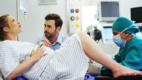 doctor examining pregnant woman during delivery while man holding her hand in operating room