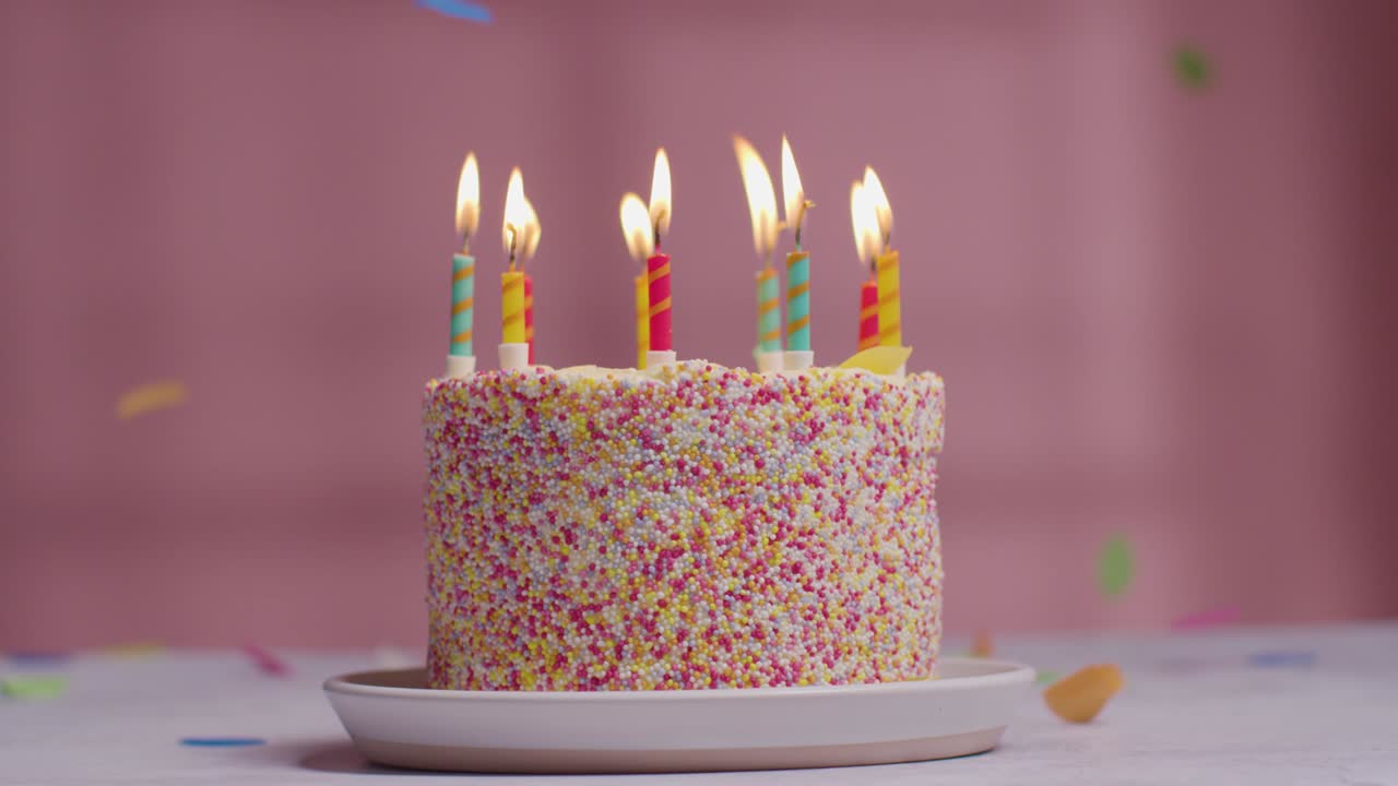 foto de estudio de confeti de papel cayendo sobre un pastel de cumpleaños cubierto con decoraciones y velas encendidas que se apagan 1