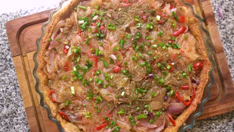 top view of uncooked onion tart with red bell pepper, spring onions, spices, and herbs