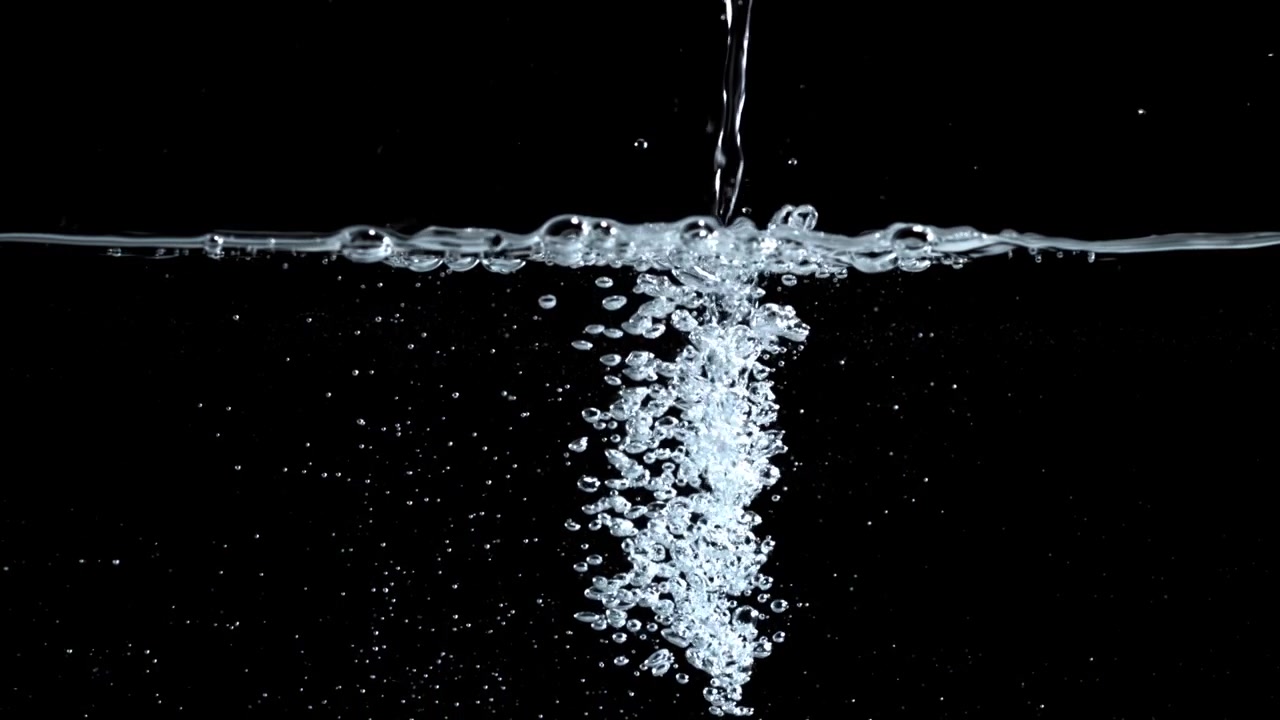 Acqua limpida che si versa nel liquido creando bolle su sfondo nero