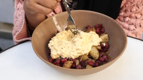 a person eating a bowl of scrambled eggs with potatoes