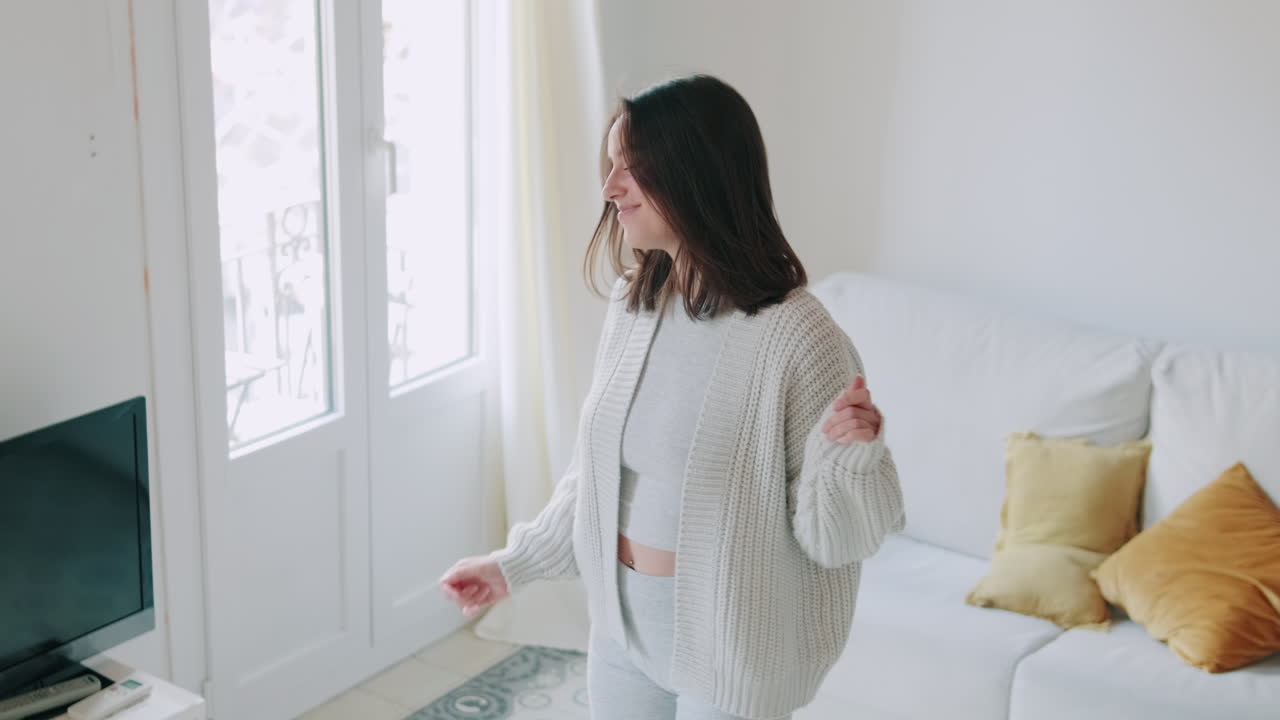 幸せな若い女性が、明るいリビングルームで楽しそうに踊る