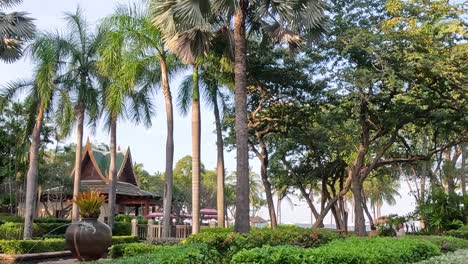 a vibrant garden scene featuring tall palm trees and dense greenery under a clear blue sky.
