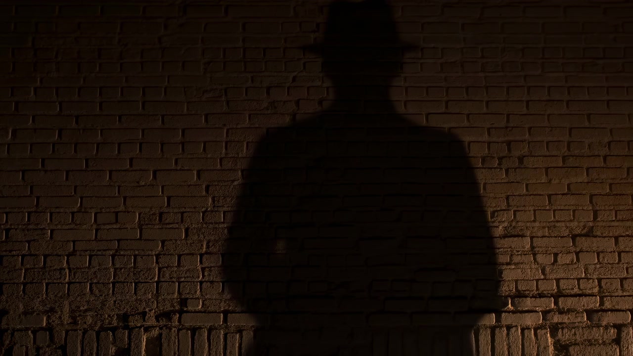 Silhueta de homem contra parede de tijolos, estranho solitário e sombrio de fedora projeta sombra alta em alvenaria texturizada
