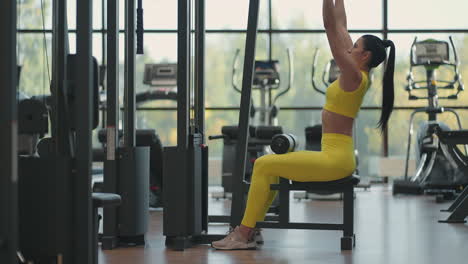 hispanic woman sitting on a simulator in the gym pulls a metal rope with the weight pumps up the muscles of the back. brunette woman pulls on simulator. performing exercise for back muscles simulator