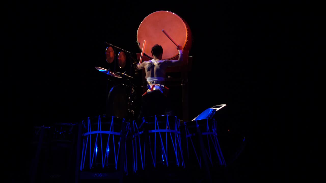Kraftfull Taiko-trommeslager opptrer på en mørk scene med blå belysning