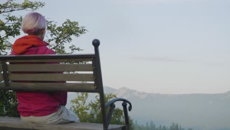 woman sitting on bench at sunrise viewing mountain scenery