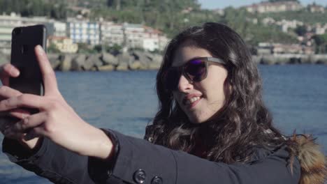 smiling girl takes selfie and pictures with smartphone near the sea