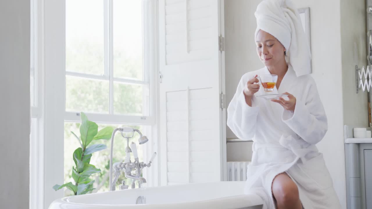 행복한 아시아 여성이 욕조에 앉아서 화장실에서 차를 마시고, 느린 움직임으로