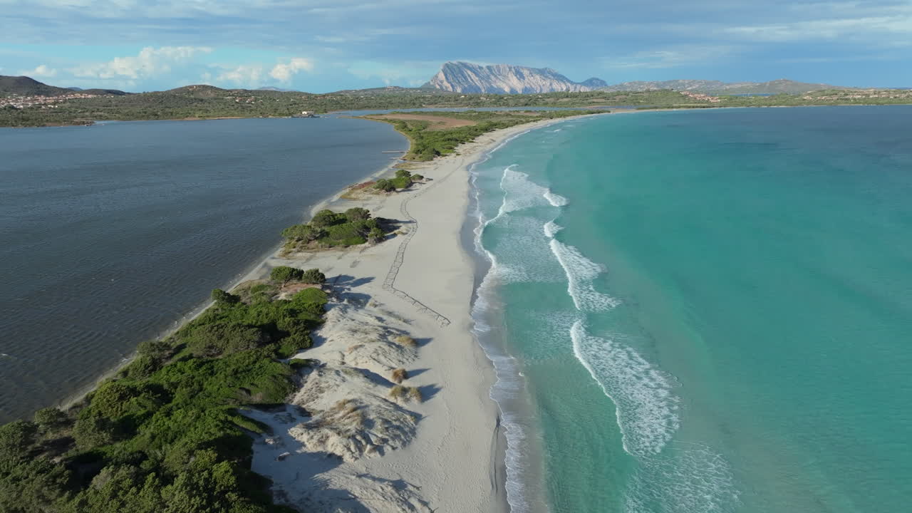 Turquoise water laps gently against the white sand of La Cinta beach in sardinia, italy, with a lagoon on one side and the tyrrhenian sea on the other