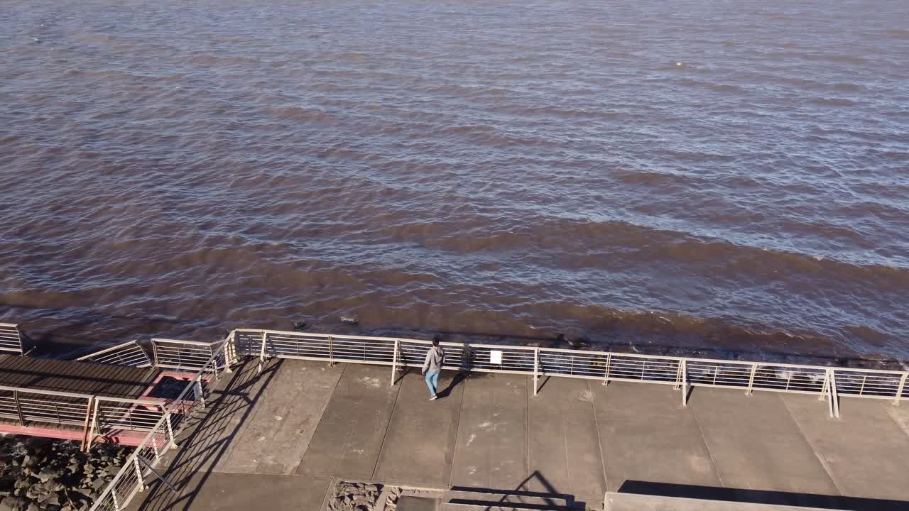 joven caminando a lo largo de las orillas del río en el pavimento de hormigón frente al mar con formas geométricas, buenos aires en argentina