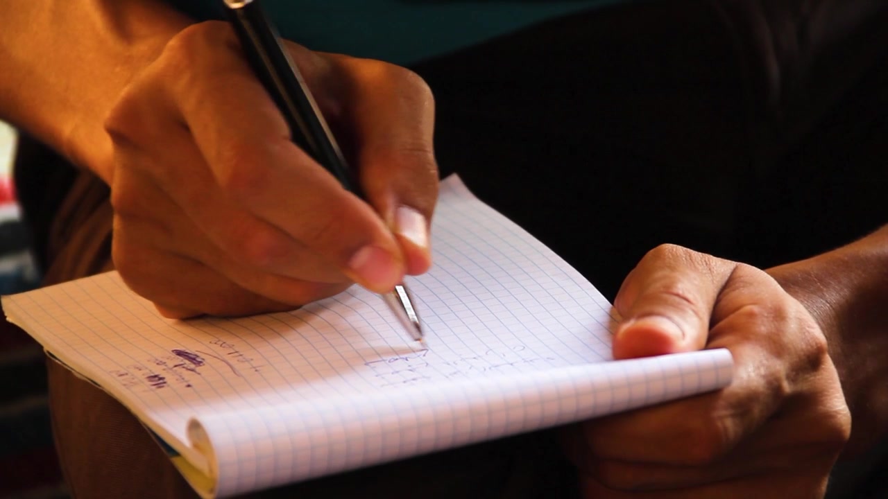 A close-up shot of a person's hands writing notes in a lined notebook with a black pen, capturing the focus and detail of the writing process.