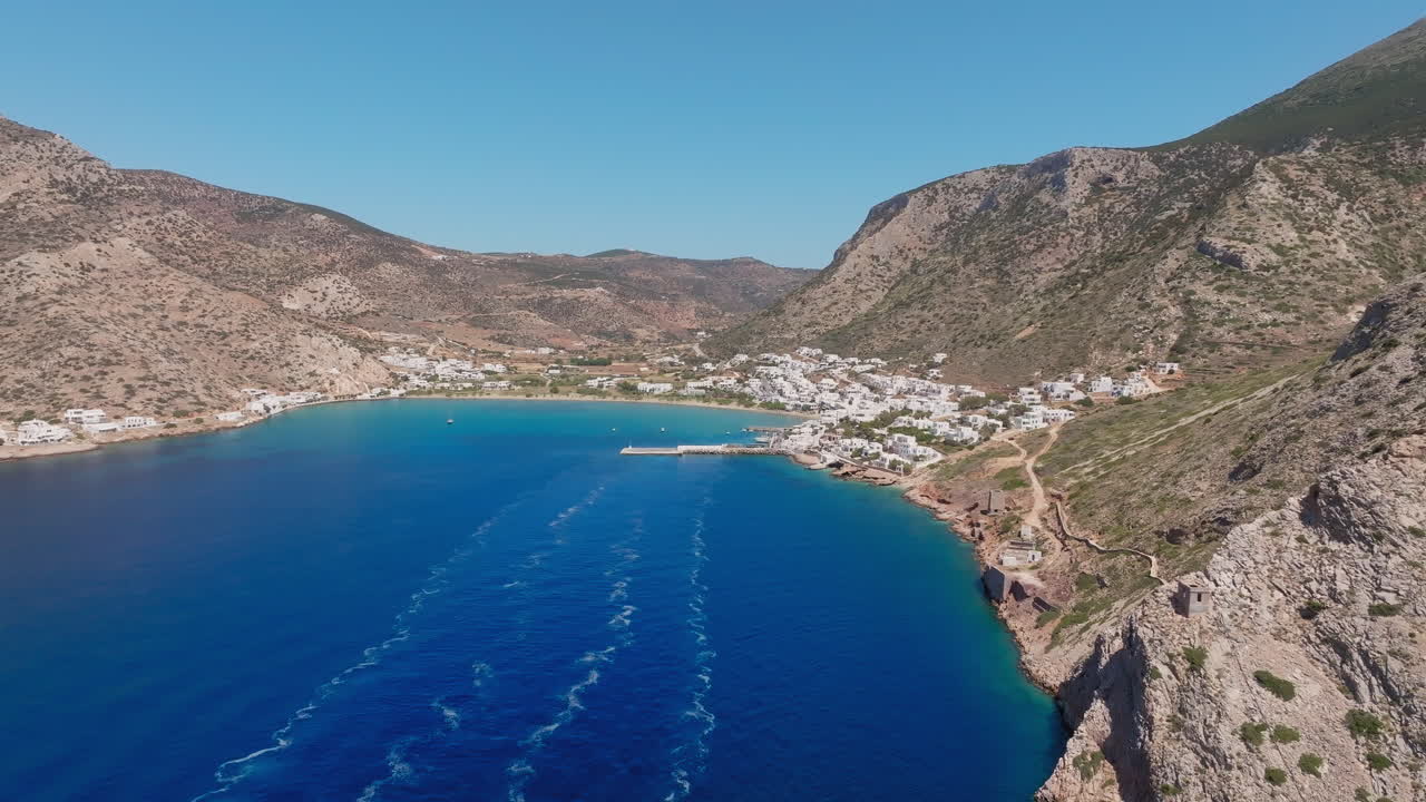 Wide aerial of Sifnos port and Kamares Bay with boats docked near shoreline, Cyclades, Greece