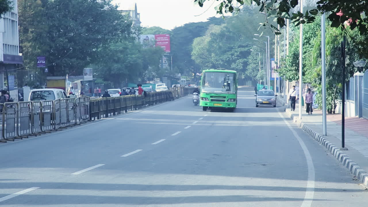 Green city bus drives on a quiet afternoon street in Bangalore with sparse traffic and trees around
